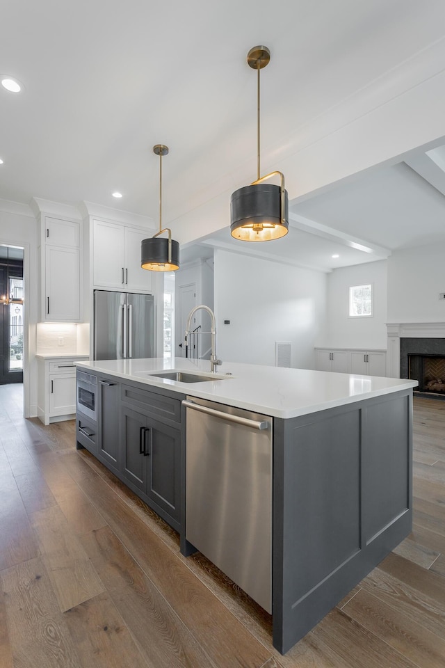 kitchen with stainless steel appliances, a sink, white cabinetry, a center island with sink, and dark wood-style floors