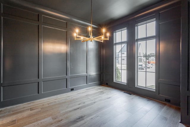 unfurnished dining area featuring a decorative wall, a chandelier, and light wood-style floors