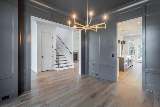 spare room with a decorative wall, a chandelier, stairway, light wood-style floors, and a sink