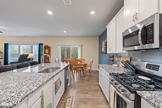 7587 Highborne Ln, Ooltewah, TN 37363 - kitchen with stainless steel appliances, a sink, light wood-style flooring, white cabinetry, and decorative backsplash