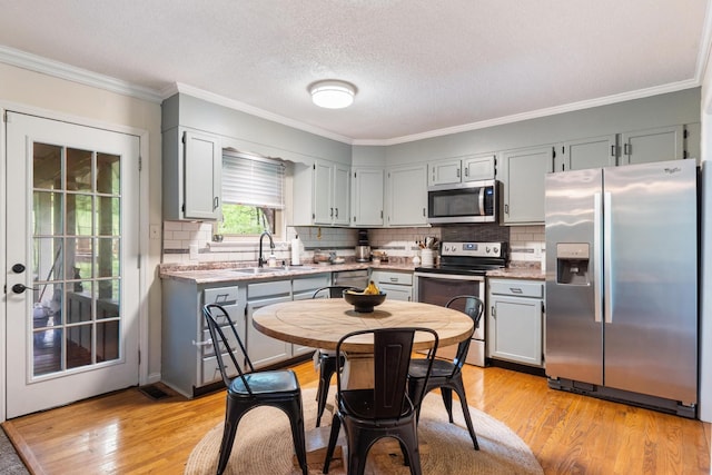 kitchen with appliances with stainless steel finishes, a sink, light wood-style floors, crown molding, and light countertops