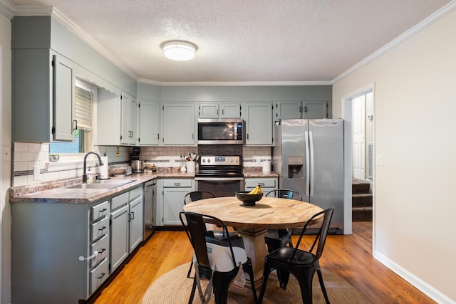 kitchen featuring appliances with stainless steel finishes, a sink, light wood finished floors, crown molding, and gray cabinets