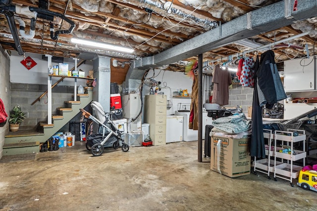unfinished basement featuring washing machine and clothes dryer, stairway, and concrete block wall