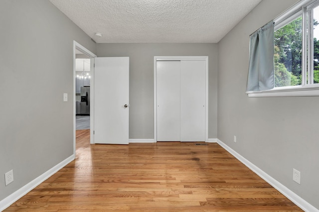 unfurnished bedroom featuring stainless steel fridge with ice dispenser, baseboards, light wood finished floors, a textured ceiling, and a closet