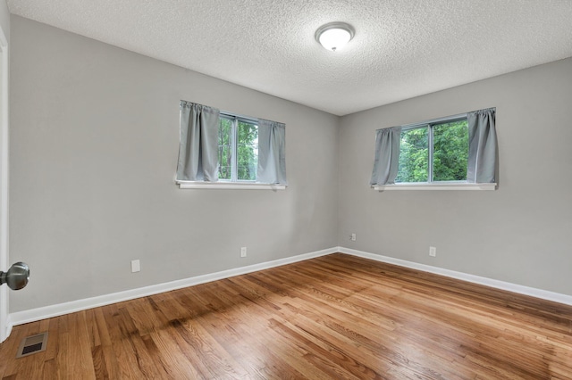unfurnished room featuring a textured ceiling, plenty of natural light, wood finished floors, and baseboards