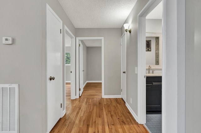 corridor featuring light wood finished floors, baseboards, a textured ceiling, and a sink