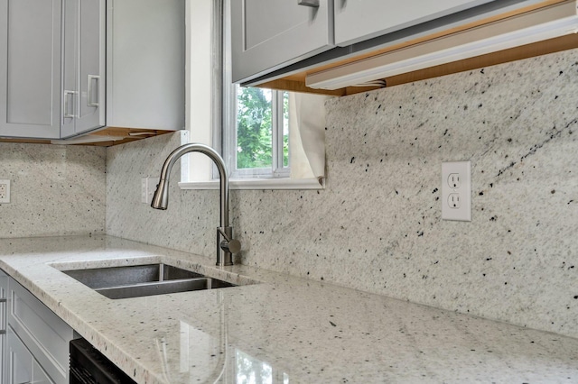 kitchen with a sink, decorative backsplash, light stone counters, and gray cabinetry