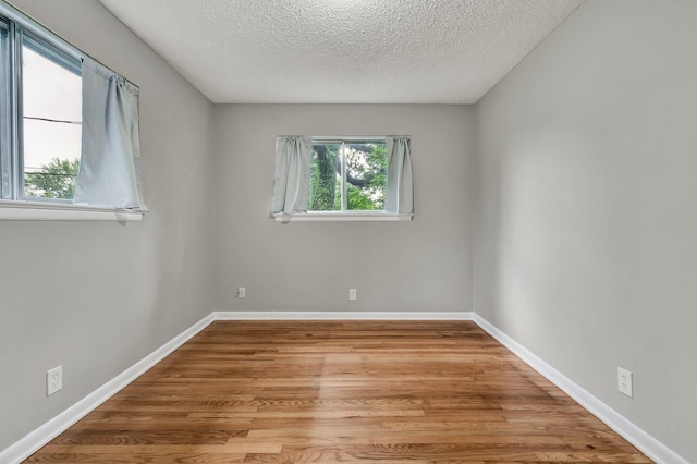 unfurnished room with a textured ceiling, light wood-style flooring, and baseboards