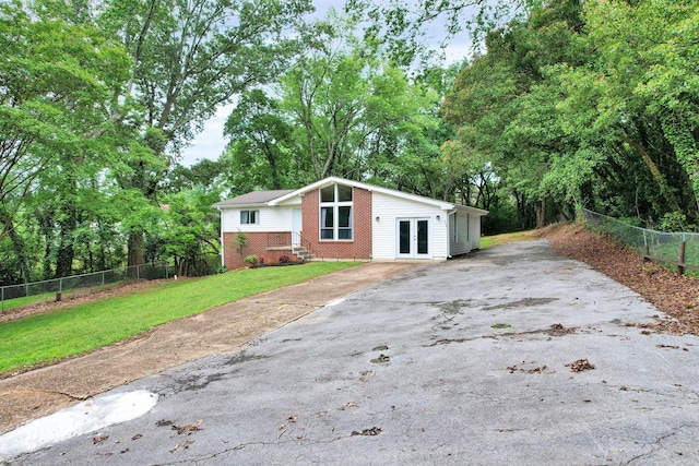 mid-century modern home featuring french doors, driveway, brick siding, and view of wooded area