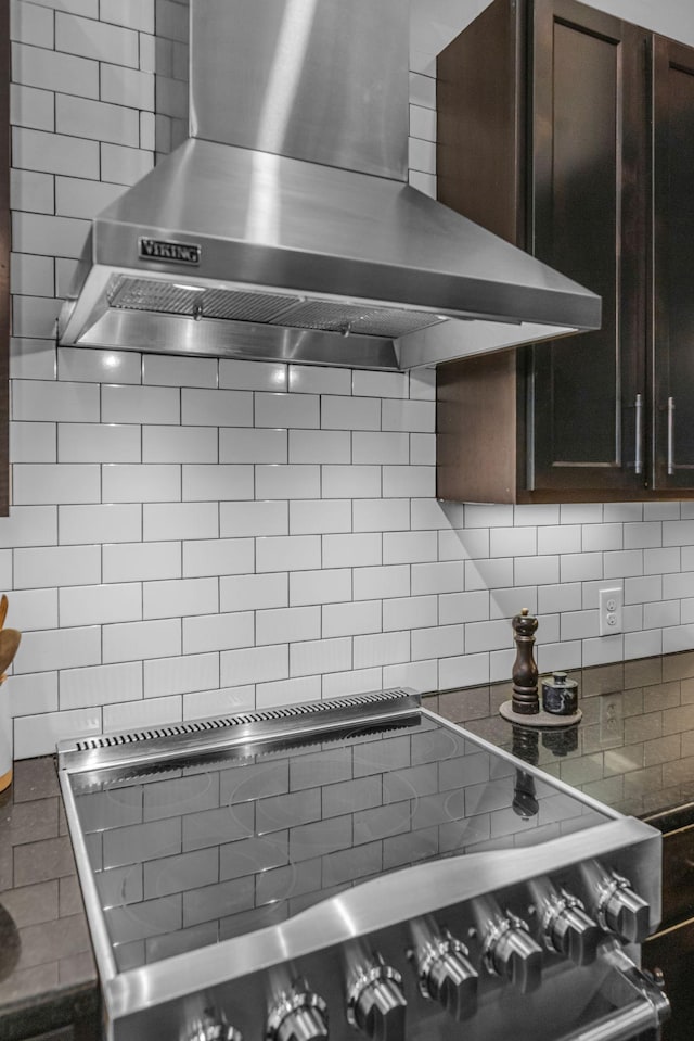 kitchen with wall chimney range hood, decorative backsplash, stove, and dark brown cabinetry