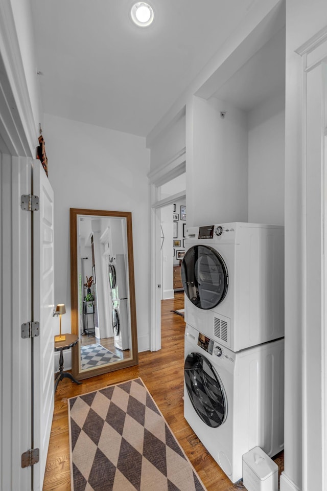 washroom with stacked washing machine and dryer, wood finished floors, and baseboards