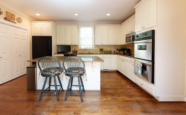 kitchen with appliances with stainless steel finishes, a sink, a center island, crown molding, and a kitchen bar