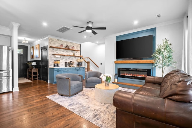 living area featuring crown molding, a ceiling fan, dark wood-style flooring, stairs, and a glass covered fireplace