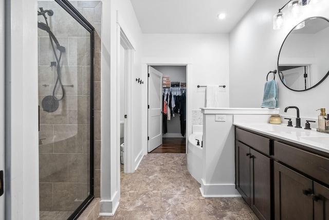 full bathroom with a shower stall, a walk in closet, vanity, a tub to relax in, and baseboards