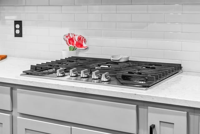 kitchen view of stainless steel gas cooktop, decorative backsplash, and light stone counters