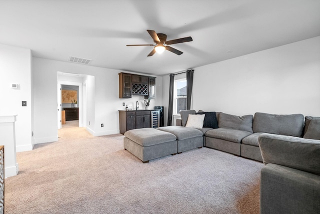 living room featuring bar with sink, ceiling fan, baseboards, and light colored carpet