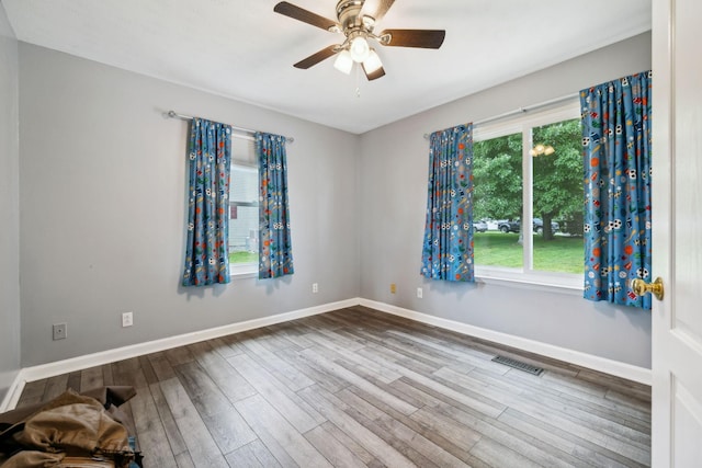 spare room with wood finished floors, a ceiling fan, and baseboards