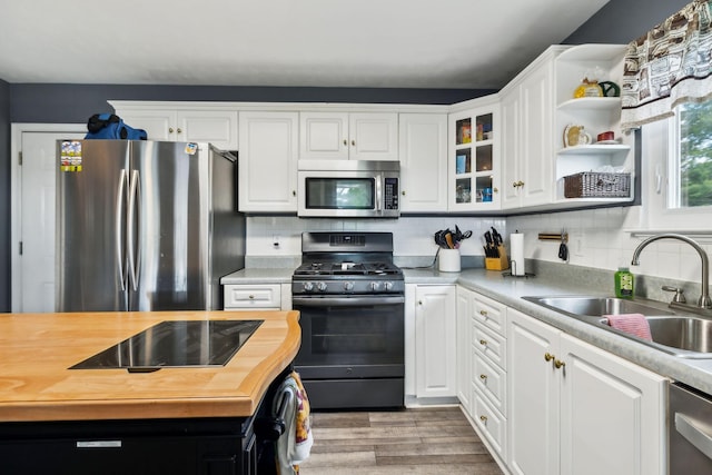 kitchen with stainless steel appliances, wooden counters, a sink, and white cabinetry