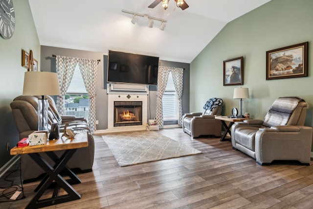 living area with ceiling fan, lofted ceiling, wood finished floors, a tile fireplace, and track lighting
