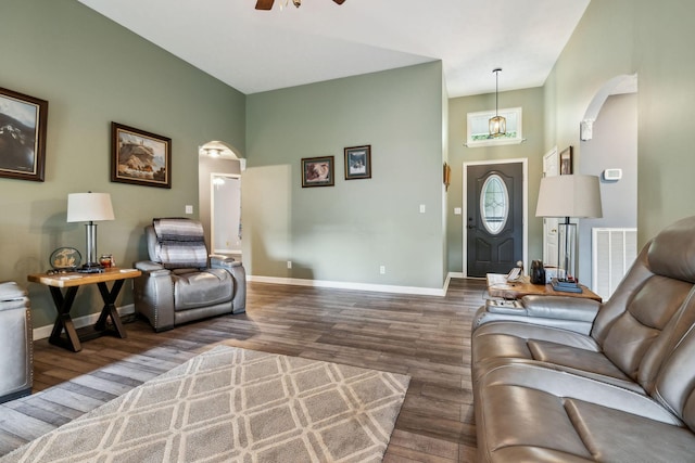 living room featuring arched walkways, wood finished floors, a ceiling fan, baseboards, and a towering ceiling