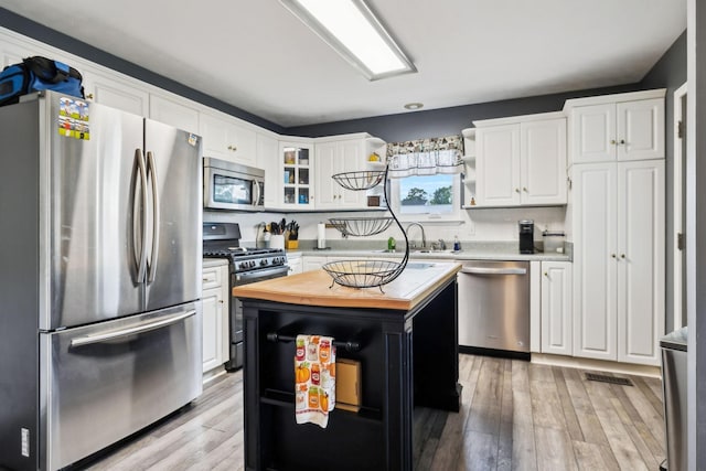 kitchen with appliances with stainless steel finishes, a sink, open shelves, wooden counters, and white cabinets