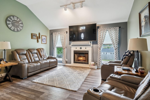 living area with lofted ceiling, wood finished floors, a tile fireplace, and track lighting