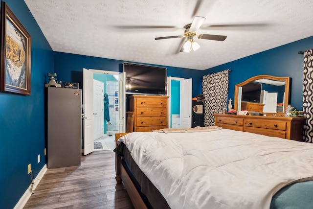 bedroom featuring a textured ceiling, wood finished floors, baseboards, ceiling fan, and ensuite bathroom