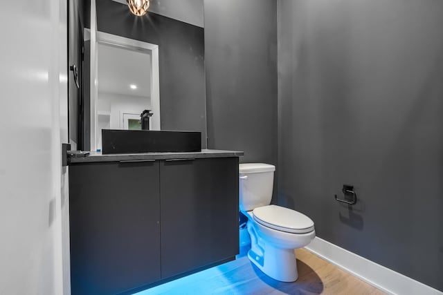 half bathroom featuring toilet, wood finished floors, vanity, and baseboards