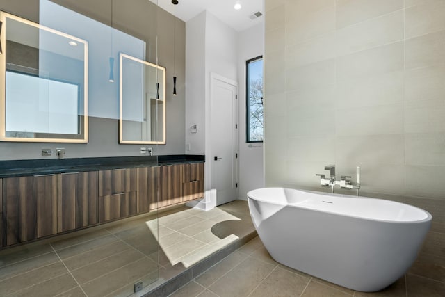 bathroom featuring a freestanding bath, double vanity, tile patterned flooring, and tile walls