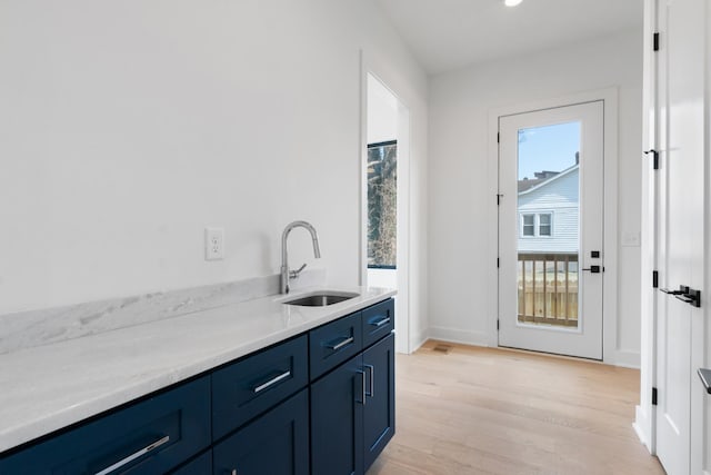 kitchen featuring a sink, blue cabinetry, light wood-style floors, light countertops, and baseboards