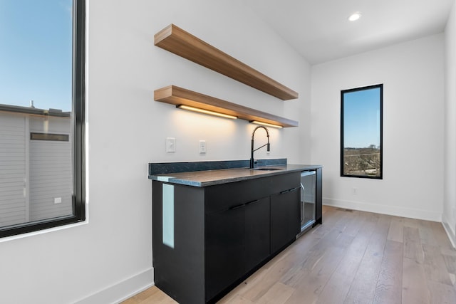 kitchen with open shelves, a sink, dark countertops, baseboards, and dark cabinetry