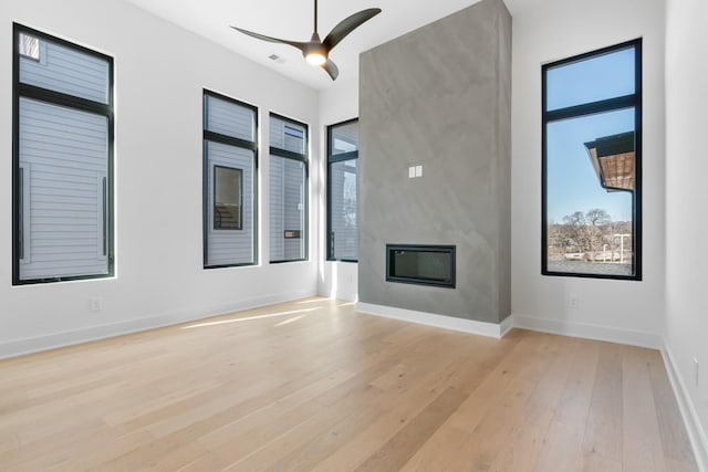 unfurnished living room with plenty of natural light, light wood finished floors, a large fireplace, and a ceiling fan