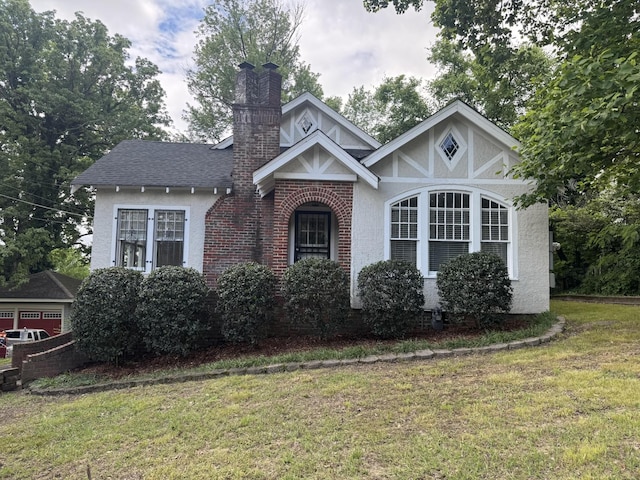 tudor-style house with a chimney, a front lawn, stucco siding, and brick siding