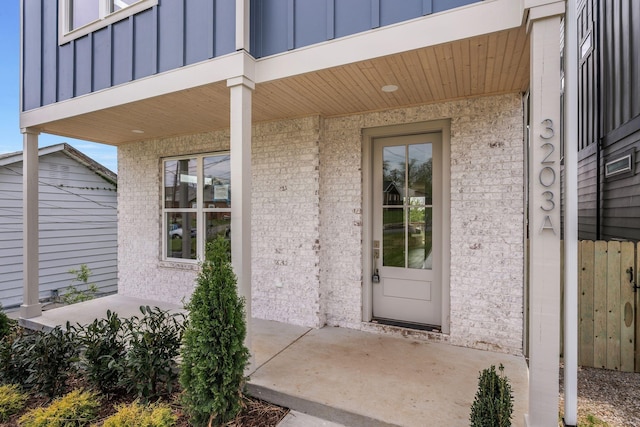 view of exterior entry featuring board and batten siding, a porch, a balcony, and brick siding