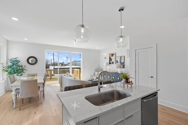 kitchen with a sink, stainless steel dishwasher, light wood finished floors, open floor plan, and baseboards