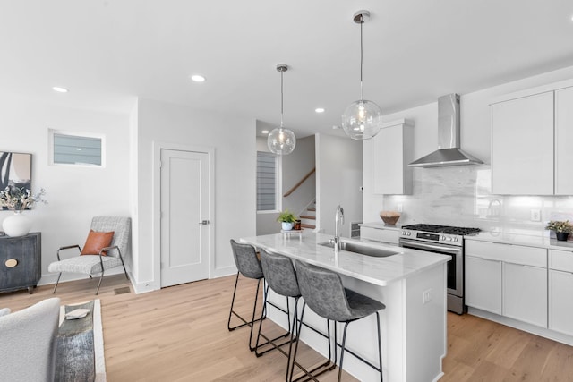 kitchen with wall chimney exhaust hood, stainless steel range with gas cooktop, a sink, light wood-style floors, and recessed lighting