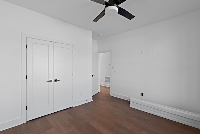 unfurnished bedroom featuring dark wood-style floors, a baseboard heating unit, baseboards, a closet, and ceiling fan