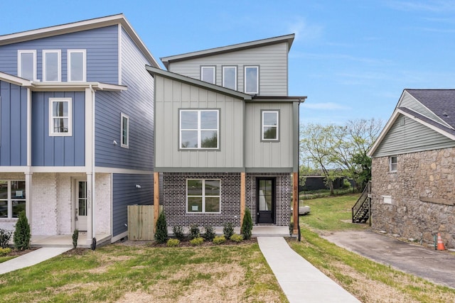 view of front of property with board and batten siding, brick siding, and a front yard