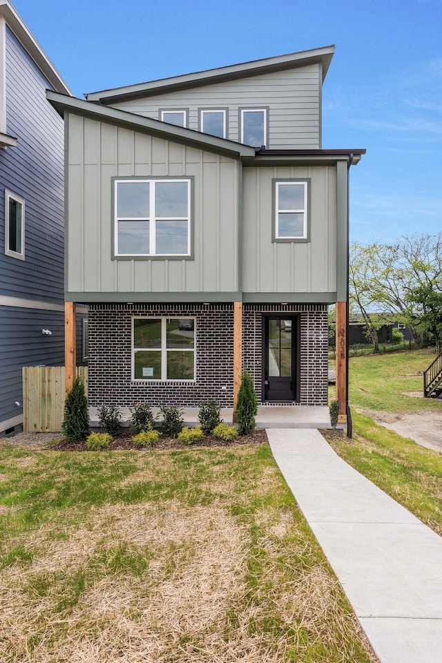 view of front of home featuring board and batten siding, brick siding, and a front yard