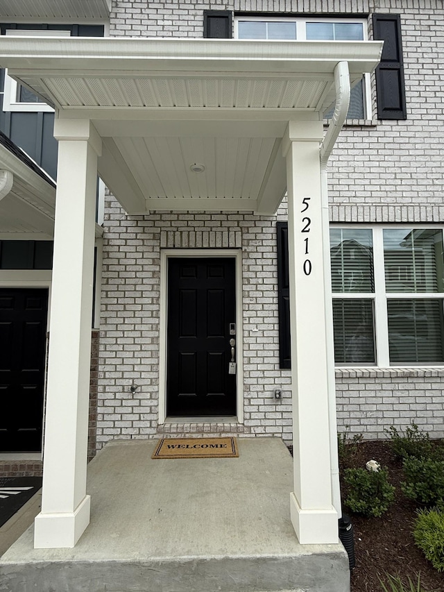 view of exterior entry featuring brick siding and covered porch