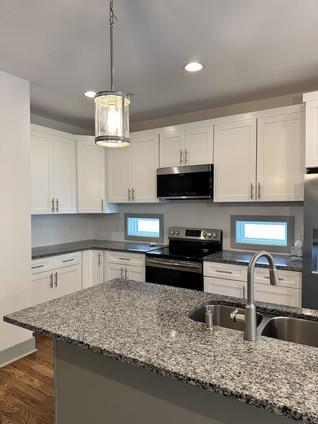 kitchen with appliances with stainless steel finishes, a sink, dark stone countertops, dark wood finished floors, and white cabinetry