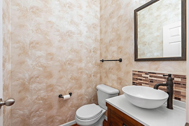 half bathroom featuring toilet, vanity, and wallpapered walls