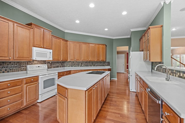 kitchen featuring white appliances, a sink, a kitchen island, light wood finished floors, and crown molding