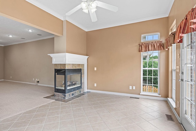 unfurnished living room featuring crown molding, a ceiling fan, a tiled fireplace, baseboards, and light tile patterned floors