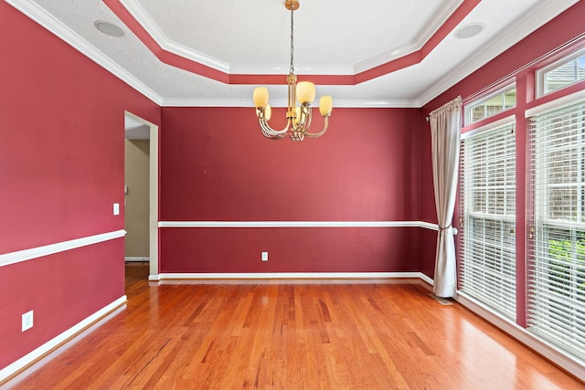empty room featuring a chandelier, a raised ceiling, wood finished floors, crown molding, and baseboards