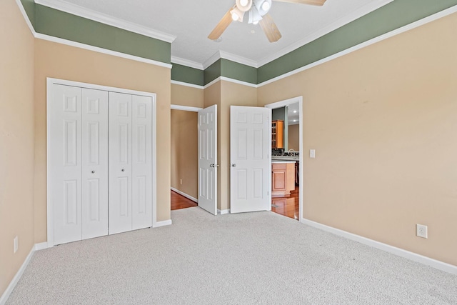 unfurnished bedroom with carpet floors, baseboards, crown molding, a closet, and a ceiling fan