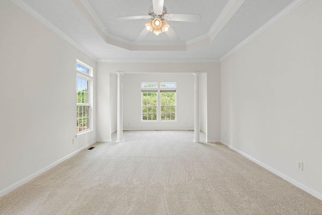 carpeted spare room featuring a raised ceiling, healthy amount of natural light, crown molding, ceiling fan, and ornate columns