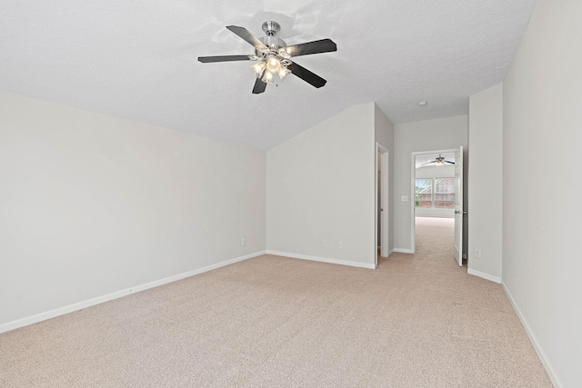 empty room featuring light colored carpet, vaulted ceiling, ceiling fan, baseboards, and a textured ceiling