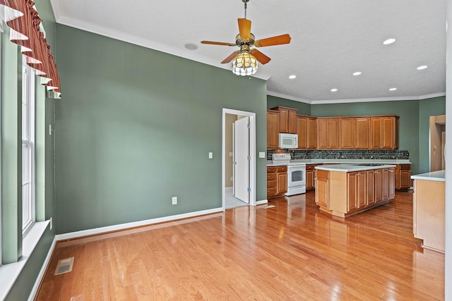 kitchen with white appliances, light wood finished floors, crown molding, backsplash, and light countertops