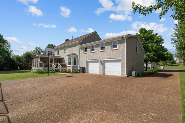 1209 Corlew Dr, Burns, TN 37029 - view of front of house with concrete driveway, a garage, central air condition unit, a sunroom, and brick siding